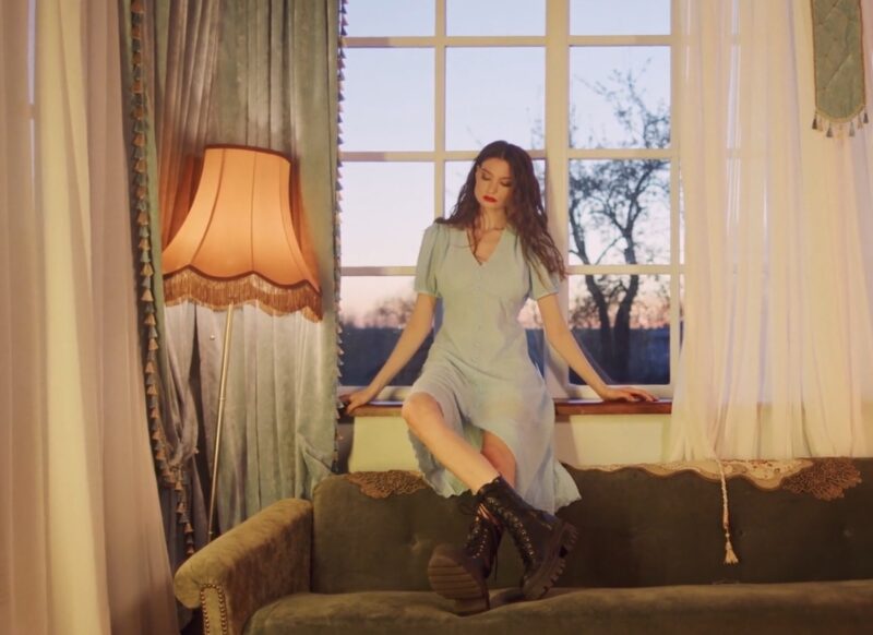 prikaz devojke u haljini i čizmama koja sedi na kauču